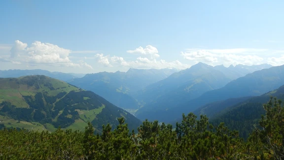 Fernblick beim Aufstieg aufs Tettensjoch Blick vom Aufstieg zum Tettensjoch über das Tal: bewaldete Hänge, dahinter gestaffelte Bergketten im Dunst.